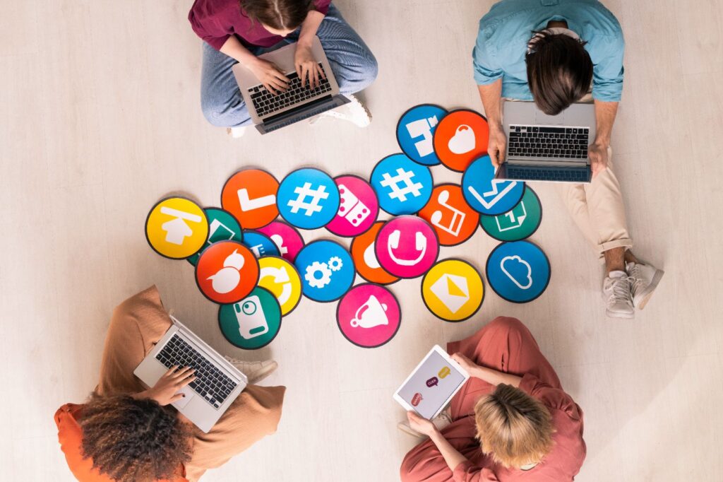 Young friendly people in casual wear sitting by multi-color papers with social media icons