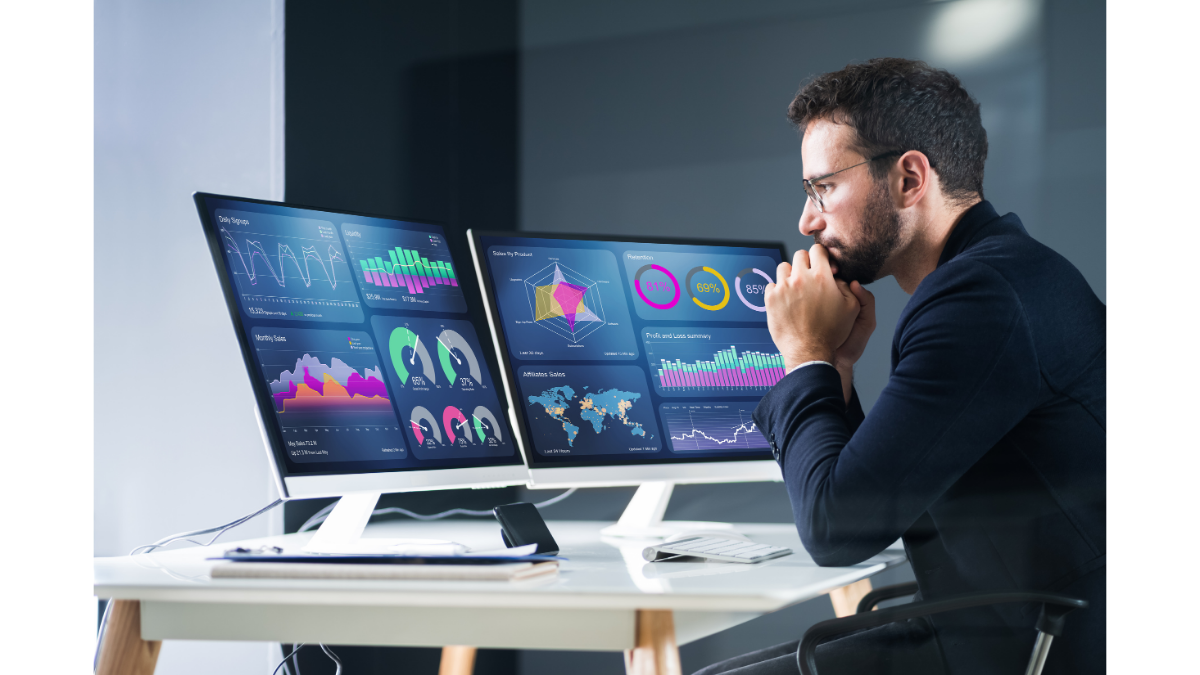 Man reviewing business intelligence dashboards and data visualizations on multiple computer screens.