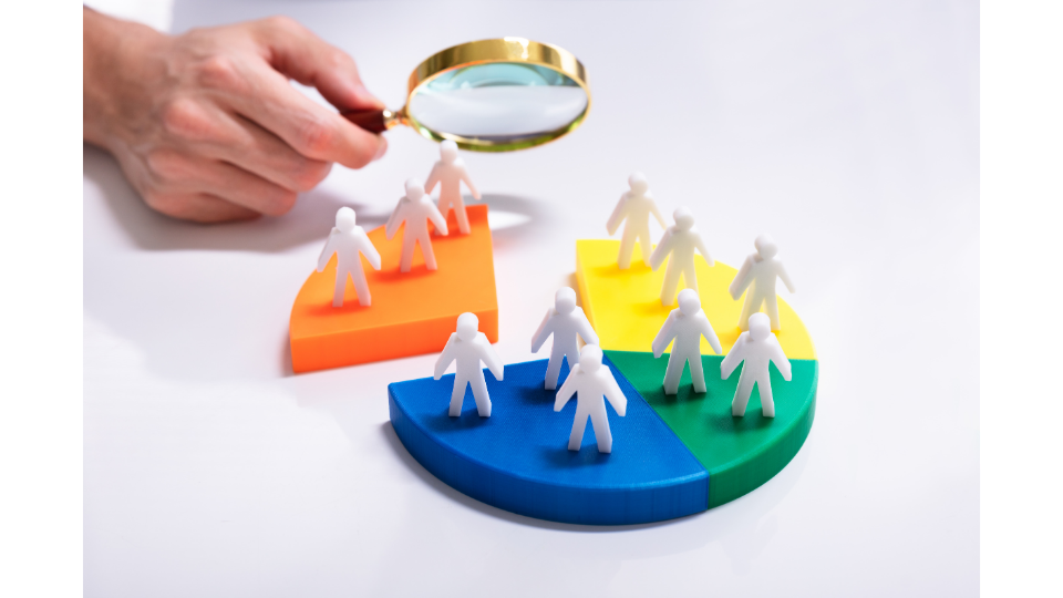 A hand using a magnifying glass to inspect human figures on a pie chart, symbolizing customer segmentation in Data-Driven Marketing to stop guessing what customers want.