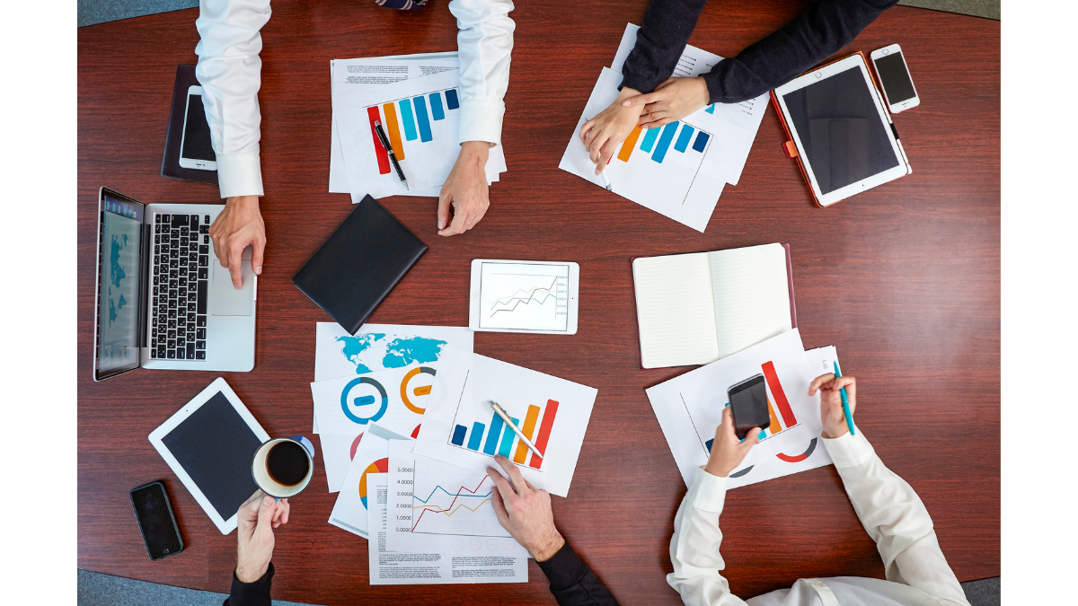Overhead view of a collaborative team analyzing charts, graphs, and digital dashboards around a table, illustrating data storytelling that transforms spreadsheets into clear, visual insights.