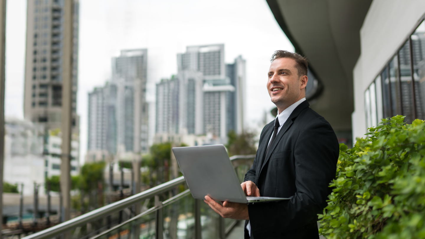 Corporate leader using a laptop to review ESG compliance and sustainable development goals against a modern city skyline.