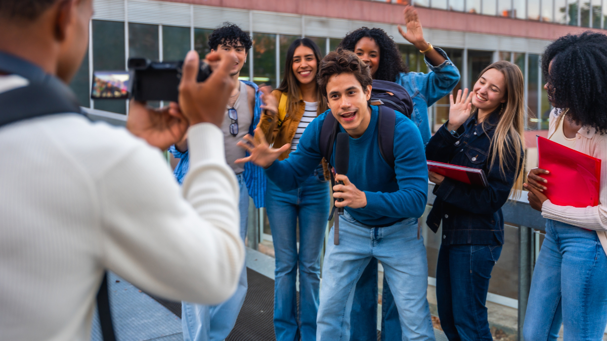 diverse group of university students, including a central host holding a microphone and a friend waving, enthusiastically engage with content creation on camera. This photo, taken from the perspectives of a peer using a handheld camera, exemplifies the raw, peer-to-peer nature of successful content seeding, showcasing how authentic user-generated content (UGC) is produced on campus for organic brand integration.