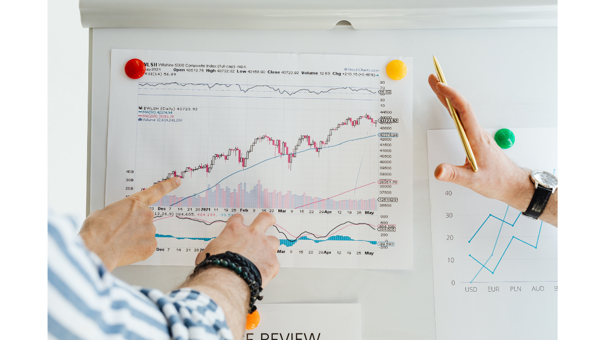 Hands pointing at a printed financial chart with trend lines and indicators on a board, representing data storytelling that turns raw spreadsheet data into meaningful visual impact.