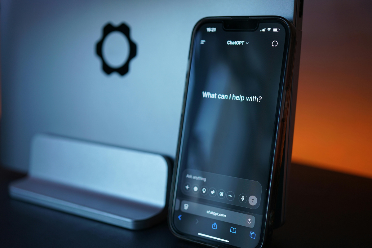 A smartphone showing the ChatGPT mobile app next to a laptop. The image represents the pervasive integration of generative AI into daily marketing workflows and the rise of AI agents in 2025.