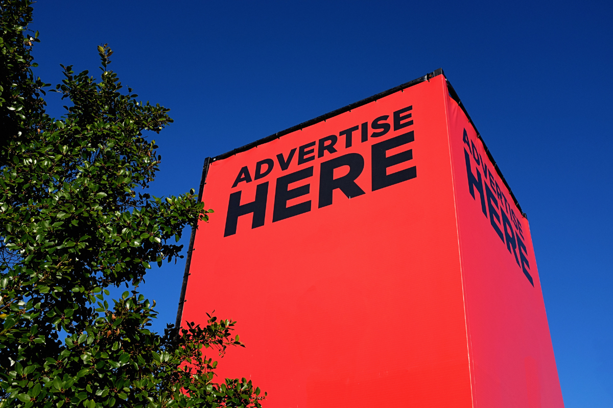 A vibrant red billboard with bold black text reading 'ADVERTISE HERE' against a clear blue sky. This represents the 2026 shift in digital advertising toward AI-powered Programmatic platforms and Predictive analytics that transform traditional ad spaces into high-precision marketing tools.
