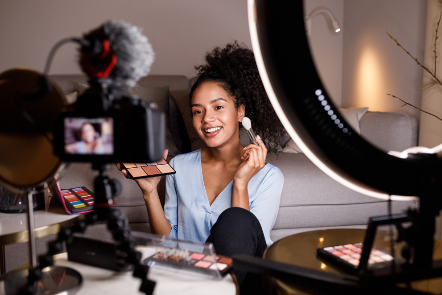 Beauty content creator filming a makeup tutorial at home with a camera and ring light, holding a makeup palette and brush, showcasing Influencer marketing through social media beauty content creation