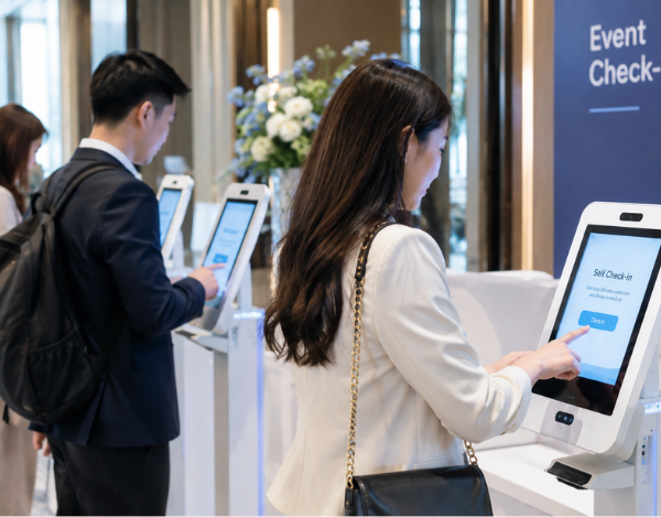 Two professional attendees using touchscreen event registration kiosks for automated self check-in at an indoor venue.