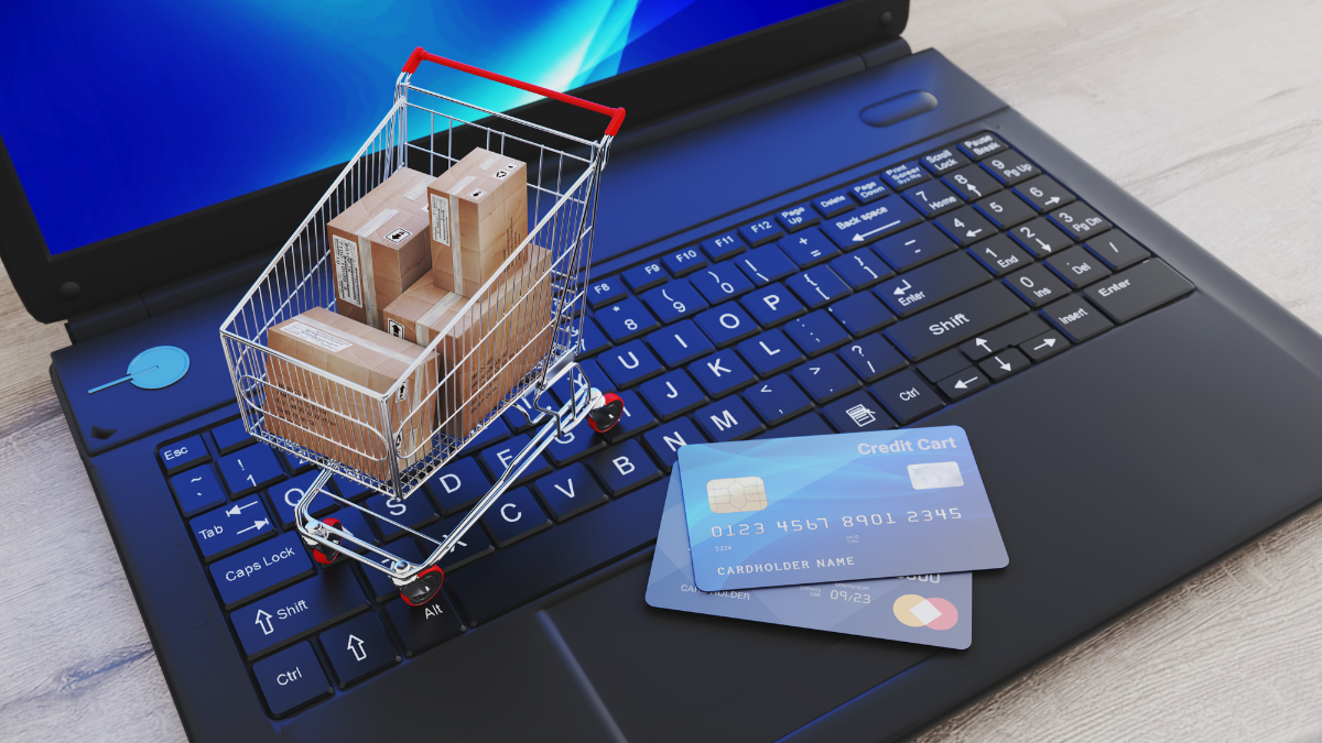 A miniature shopping cart filled with cardboard boxes and two credit cards resting on a laptop keyboard, illustrating the concept of social commerce.